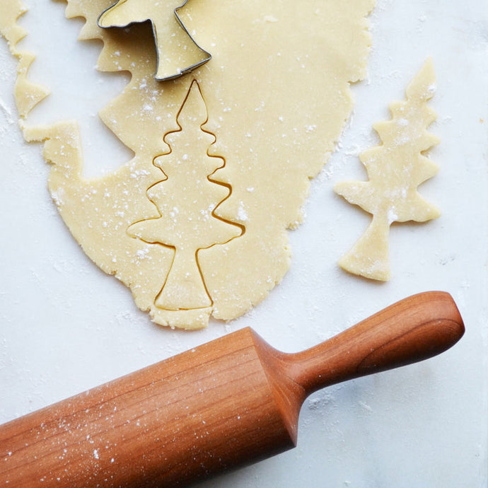 rolling pin next to dough being cut into christmas tree design